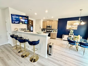Een moderne keuken met een centraal eiland, barstoelen en een eethoek met een kroonluchter.