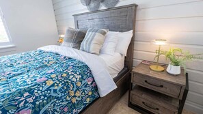 A bed with a floral comforter, a wooden headboard, and a bedside table with a lamp and a plant. - New 2br - Pool Patio - Bunk Beds - 1st Floor 2 Bedroom Apts (South Padre Island)