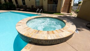 Un bain à remous avec un bord carrelé, une piscine et des chaises longues.