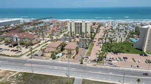 A coastal hotel area with a parking lot, buildings, and a view of the ocean. - New 2br - Pool Patio - Bunk Beds - 1st Floor 2 Bedroom Apts (South Padre Island)