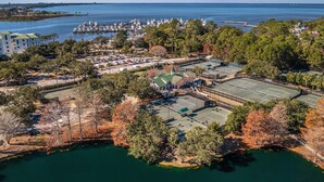 Eine Luftaufnahme einer Küstenlandschaft mit einem Yachthafen, Tennisplätzen und einem großen Gebäude mit Gründach.