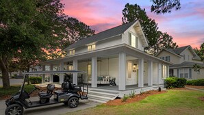 Ein zweistöckiges Haus mit überdachter Veranda, einem Golfwagen und einem gepflegten Rasen.