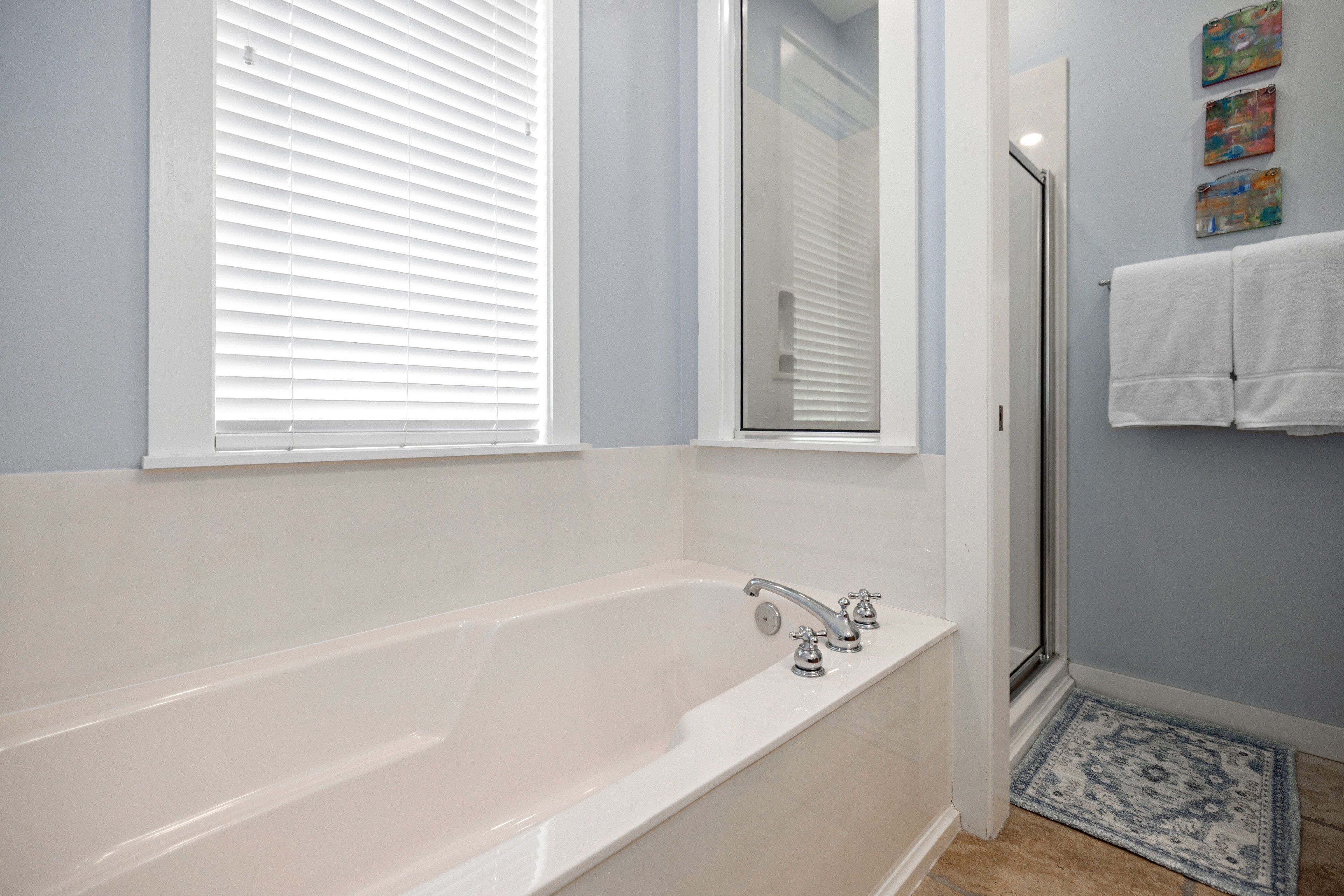 Ein Badezimmer mit Badewanne, Dusche, einem Fenster mit Jalousien, einem Spiegel und einem Teppich.