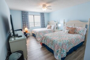 Une chambre avec deux lits, un bureau, une chaise, un ventilateur de plafond et une fenêtre avec des rideaux.