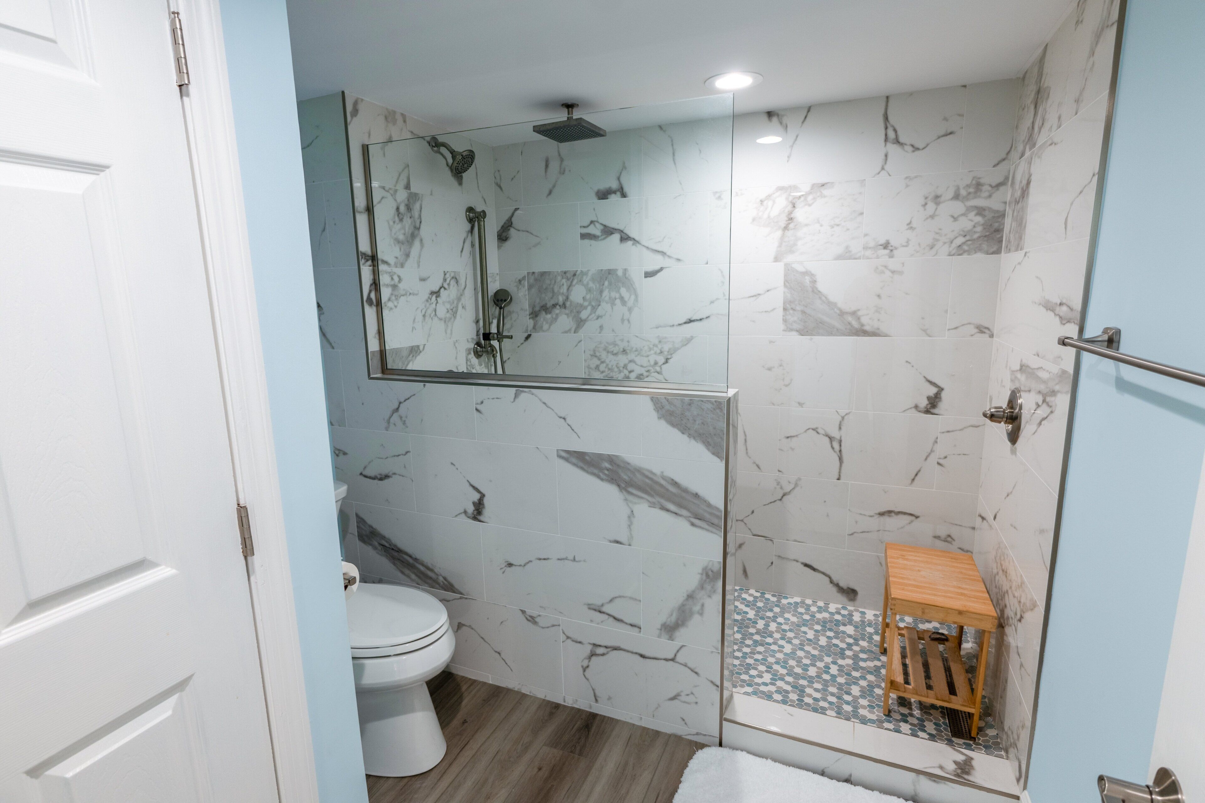 Une salle de bain avec une douche à parois de verre, des toilettes et un petit tabouret en bois.