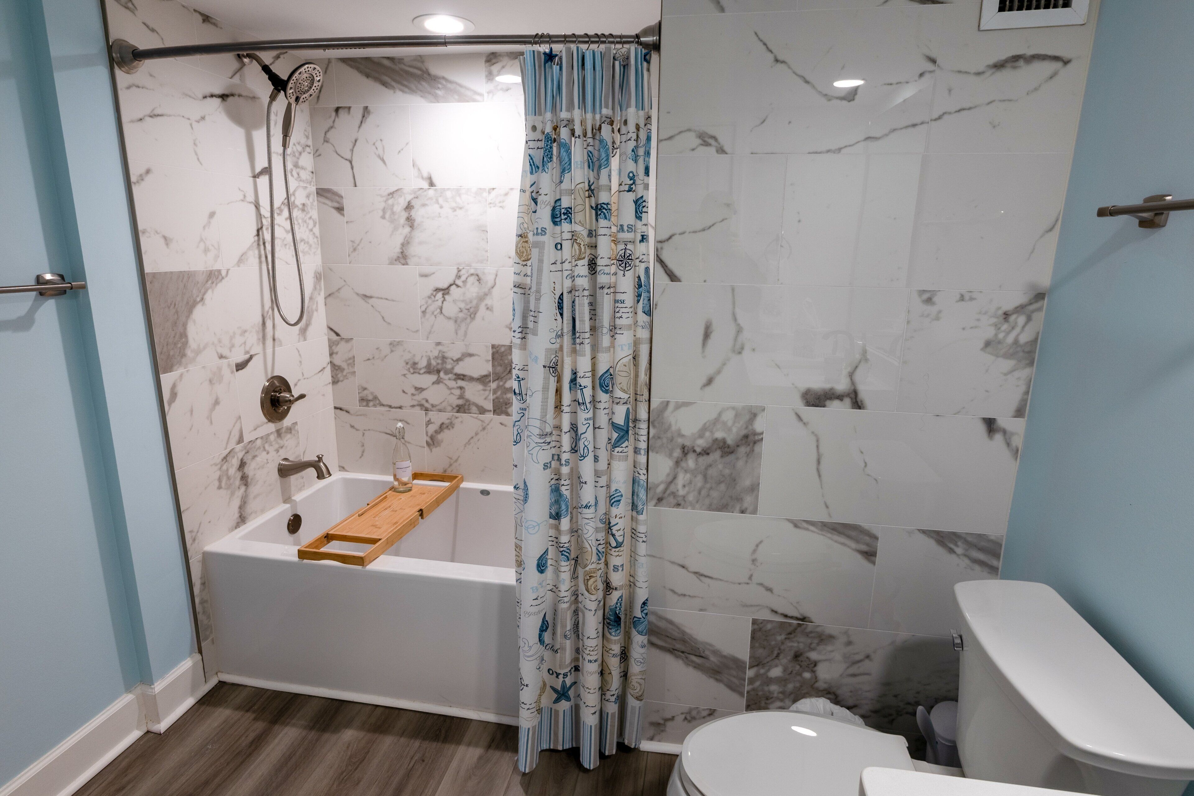 A bathroom with a bathtub, shower, toilet, and marble tiles.