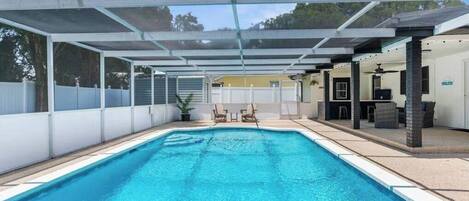 A swimming pool with a covered area, lounge chairs, and a patio with outdoor furniture.
