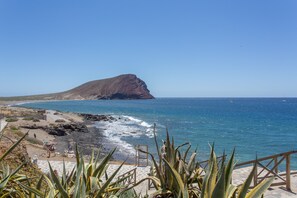 Un paysage côtier caractérisé par un promontoire rocheux, une plage de sable et une mer d’un bleu limpide.