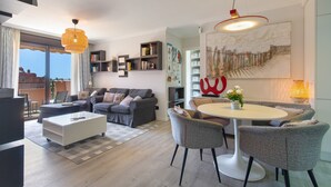 A modern living room with a sofa, coffee table, and chairs, a bookshelf, and a dining area with a table and chairs. - Vacation Apartment 'Veras Home' with Sea View, Wi-Fi and Air Conditioning (La Tejita)