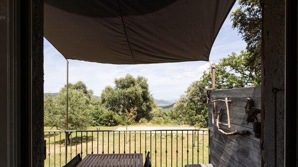 Patio esterno con tavolo e sedie, parete in legno con una scala e vista su alberi e colline.