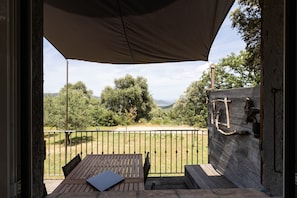 Eine Außenpatio mit Tisch und Stühlen, eine Holzwand mit einer Leiter und Blick auf Bäume und Hügel.