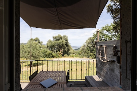 An outdoor patio with a table and chairs, a wooden wall with a ladder, and a view of trees and hills.