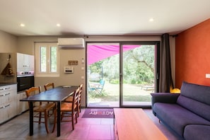 A modern kitchen with a dining area, a sofa, and a sliding glass door leading to a garden. - Holiday Home “Gîte Alcido” with Sea View, Wi-Fi and Air Conditioning (Muro)