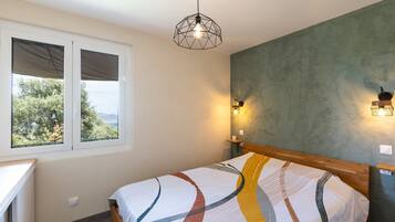 Une chambre à coucher avec un lit, une fenêtre avec des stores, un luminaire fixé au mur et un autre suspendu au plafond.