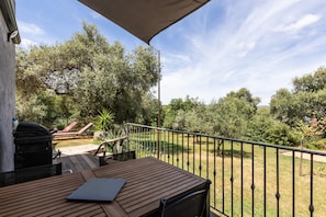 Eine Holzterrasse mit Tisch und Stühlen, einem Grill und Blick auf eine Rasenfläche mit Bäumen.