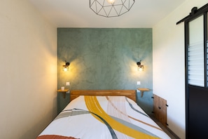 A bedroom with a bed, two wall-mounted lights, a wooden headboard, and a window with blinds. - Holiday Home “Gîte Alcido” with Sea View, Wi-Fi and Air Conditioning (Muro)