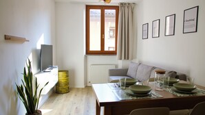 En matplats med ett bord dukat för fyra personer, en soffa, en krukväxt och ett fönster med gardiner.