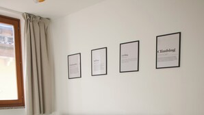Ett rum med en grå soffa, ett matbord i trä med stolar och inramade tavlor på väggen.