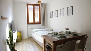Ett sovrum med en säng, ett fönster med gardiner, ett sängbord, en sänglampa, en krukväxt och en matplats med ett bord och stolar.