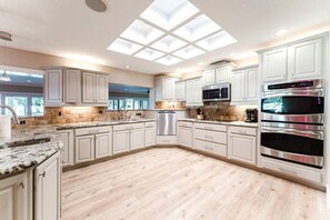 A modern kitchen with white cabinets, a stainless steel refrigerator, a double oven, and a skylight. - Indian Rocks Escape Luxury Beach Villa Pickleball, Pool & Game Room (Largo)