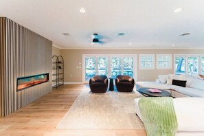 A modern living room with a fireplace, two armchairs, a sofa, and a view of a swimming pool through large windows. - Indian Rocks Escape Luxury Beach Villa Pickleball, Pool & Game Room (Largo)