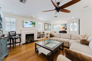 A living room with a fireplace, sofa, coffee table, and ceiling fan. - Coco Plum Cottage a Charming Retreat Htd Pool and BBQ (West Palm Beach)