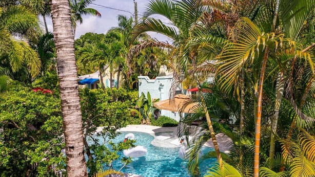 Ein Pool, umgeben von tropischer Vegetation, und ein Gebäude mit einem Reetdach.