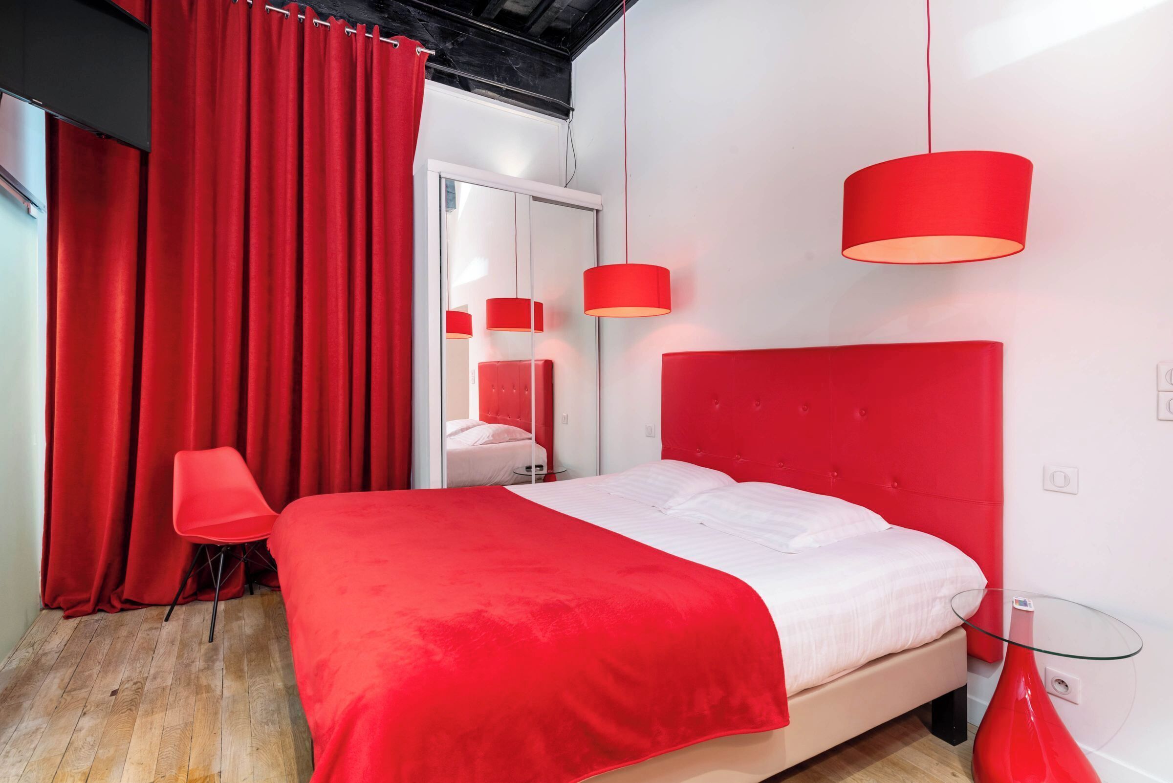 Une chambre moderne avec une couvre-lit rouge, une table en verre et une chaise rouge.