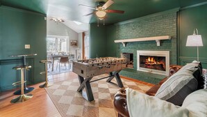 A cozy room with a foosball table, a fireplace, and a ceiling fan. - 3000sqft 5B3.5B Retreat Near Lenovo Center - Upscale 3 King Beds (Cary)