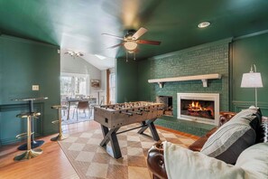 A room with a foosball table, a fireplace, a ceiling fan, and a bar area.