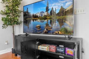 A flat-screen TV on a wooden stand, a potted plant, and a shelf with snack boxes.