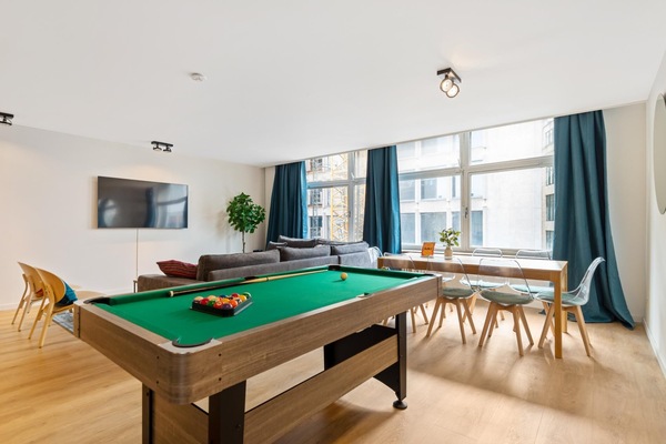 Large open living space with a pool table for casual games and a comfortable lounge area to relax. Floor to ceiling windows bring in plenty of daylight, while the dining table by the window offers a bright spot for meals or work.