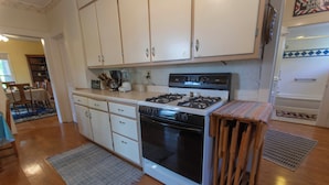 Una cocina con armarios blancos, estufa, horno y una pequeña mesa de madera.