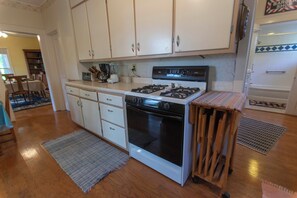 A kitchen with white cabinets, a stove, an oven, and a small wooden table. - 4-bedroom Lakefront Retro Cottage on Lake George in Fremont, IN (Fremont)