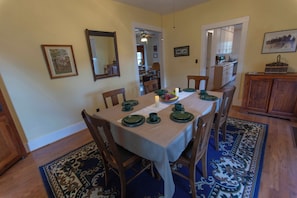 A dining area with a table set for four, surrounded by chairs, with a kitchen in the background. - 4-bedroom Lakefront Retro Cottage on Lake George in Fremont, IN (Fremont)