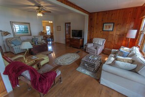 A spacious living room with a high ceiling, wooden walls, and a variety of seating options including a sofa, armchairs, and a loveseat. - 4-bedroom Lakefront Retro Cottage on Lake George in Fremont, IN (Fremont)