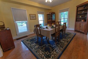 A dining room with a table set for four, surrounded by chairs, a wooden cabinet, and a patterned rug.