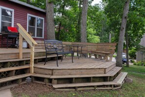 A wooden deck with a bench and a grill, surrounded by trees. - 4-bedroom Lakefront Retro Cottage on Lake George in Fremont, IN (Fremont)
