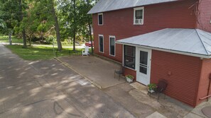 A red building with a covered porch, a small garden with potted plants, and a bench.