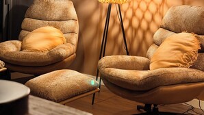 Un salon moderne avec deux fauteuils, une lampe sur pied et un mur orné d’un motif.