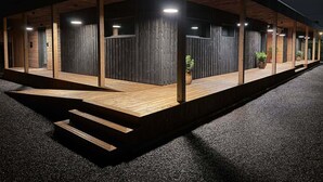 Un bâtiment moderne à l’extérieur en bois, doté de grandes fenêtres et d’un espace extérieur couvert, accessible par un escalier menant à l’entrée.