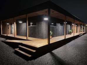 A modern building with a wooden exterior, large windows, and a covered outdoor area with steps leading to the entrance.