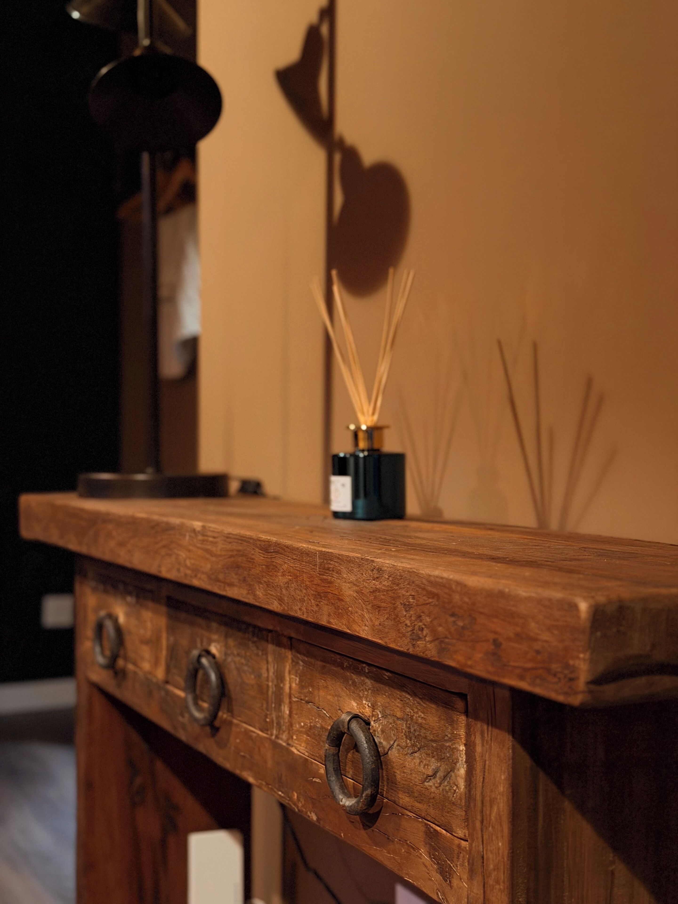 A wooden dresser with three drawers and a small bottle of reed diffuser on top.