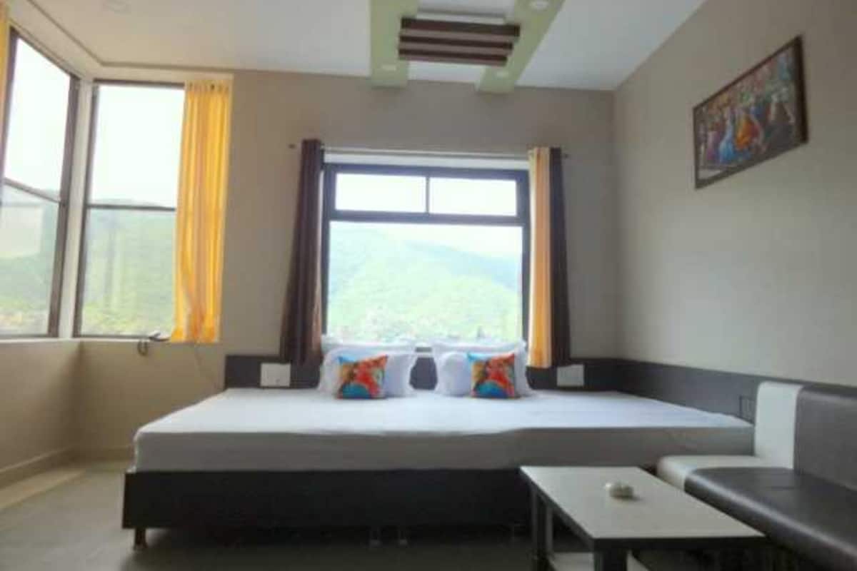 Habitación de hotel con una cama, una mesita, una ventana con cortinas y un cuadro en la pared.