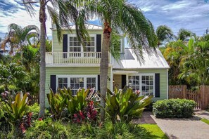 A two-story house with a balcony, surrounded by lush tropical vegetation. - Charleston House | Heated Pool and Screened Porch (West Palm Beach)