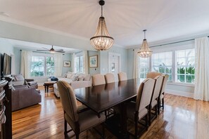 A spacious dining area with a large table and chairs, a sofa, and two chandeliers. - Charleston House | Heated Pool and Screened Porch (West Palm Beach)