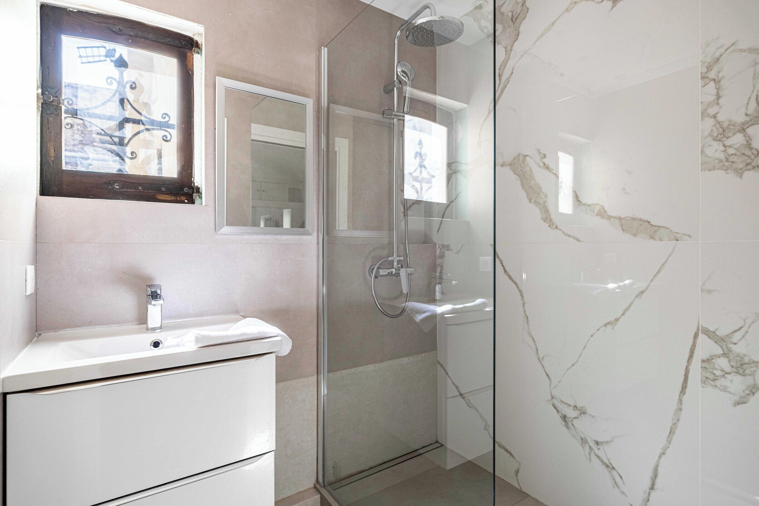 Un baño con cabina de ducha de vidrio, un lavamanos blanco y un espejo sobre él.