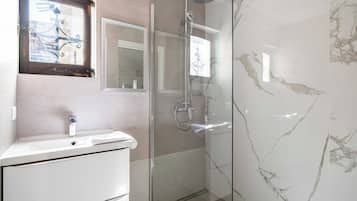 Un baño con cabina de ducha de vidrio, un lavamanos blanco y un espejo sobre él.