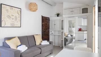 Una sala de estar moderna con un sofá gris, una obra de arte enmarcada, una lámpara de techo tejida y vistas a la cocina.