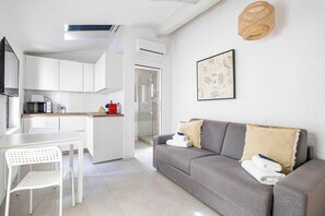 A modern living room with a grey sofa, white dining table, and a kitchen area with white cabinets. - A/C Studio in the Heart of Cannes - Old Port (Cannes)